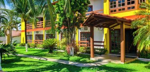A multi-story building with a vibrant yellow facade, a covered outdoor seating area, and lush greenery. - Bem Bahia Hotel (Santa Cruz Cabralia)