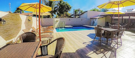 A poolside area with wicker furniture, yellow umbrellas, and a tiled floor.