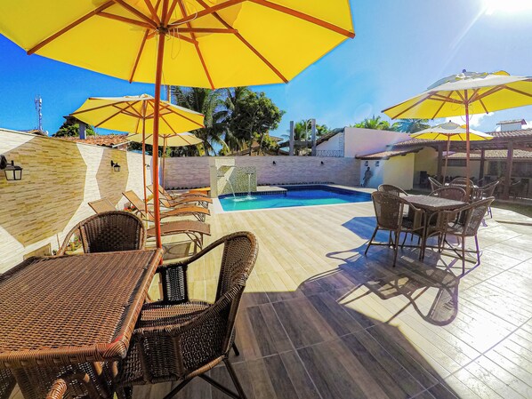 A poolside area with wicker furniture, yellow umbrellas, and a tiled floor. - Bem Bahia Hotel (Santa Cruz Cabralia)