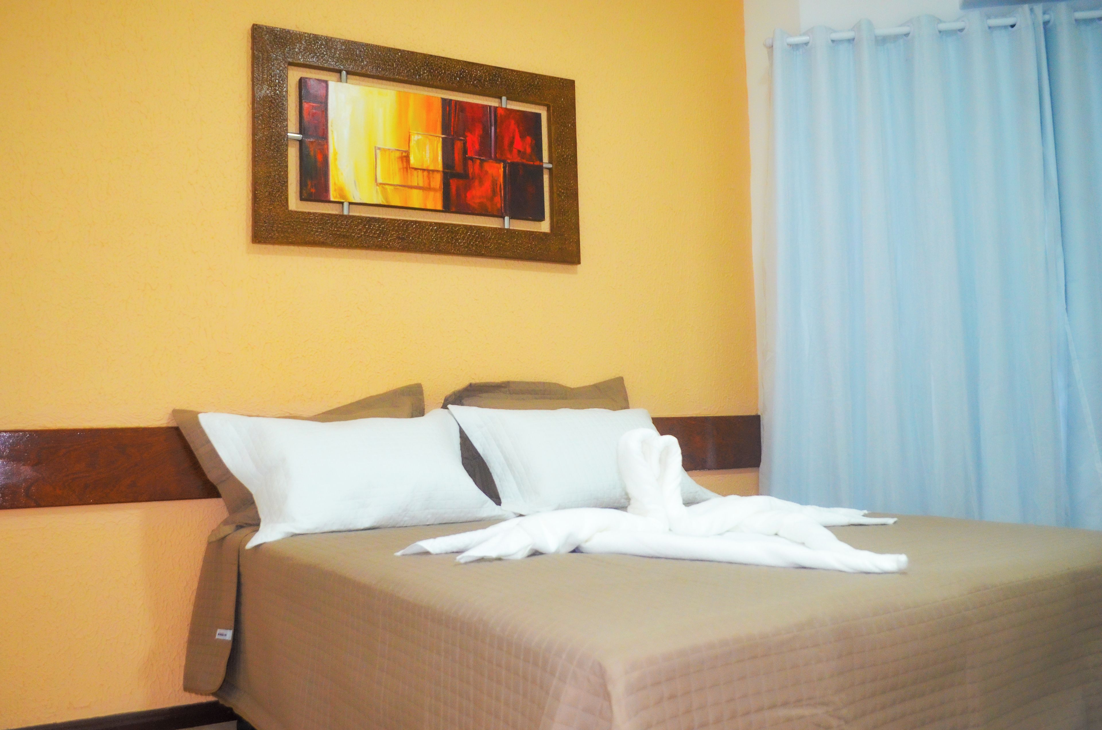 Una habitación de hotel con una cama, almohadas, una colcha y un cuadro en la pared.