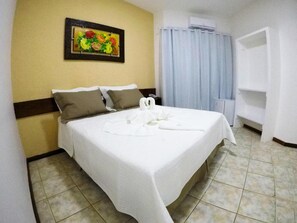 Una cama bien hecha con sábanas blancas, un cuadro floral en la pared y una cortina azul claro.