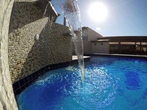 Una piscina con elemento acquatico, circondata da un muro piastrellato e un edificio.
