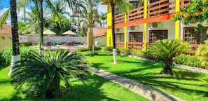 Un cortile alberato di un hotel con piscina, arredi esterni e rigogliosa vegetazione.