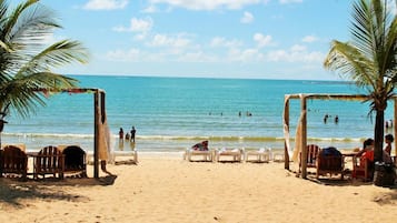 Une plage avec une structure en bois, des palmiers et des chaises de plage.