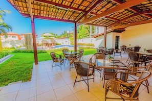 Área de varanda externa com móveis de vime e vista para uma piscina.