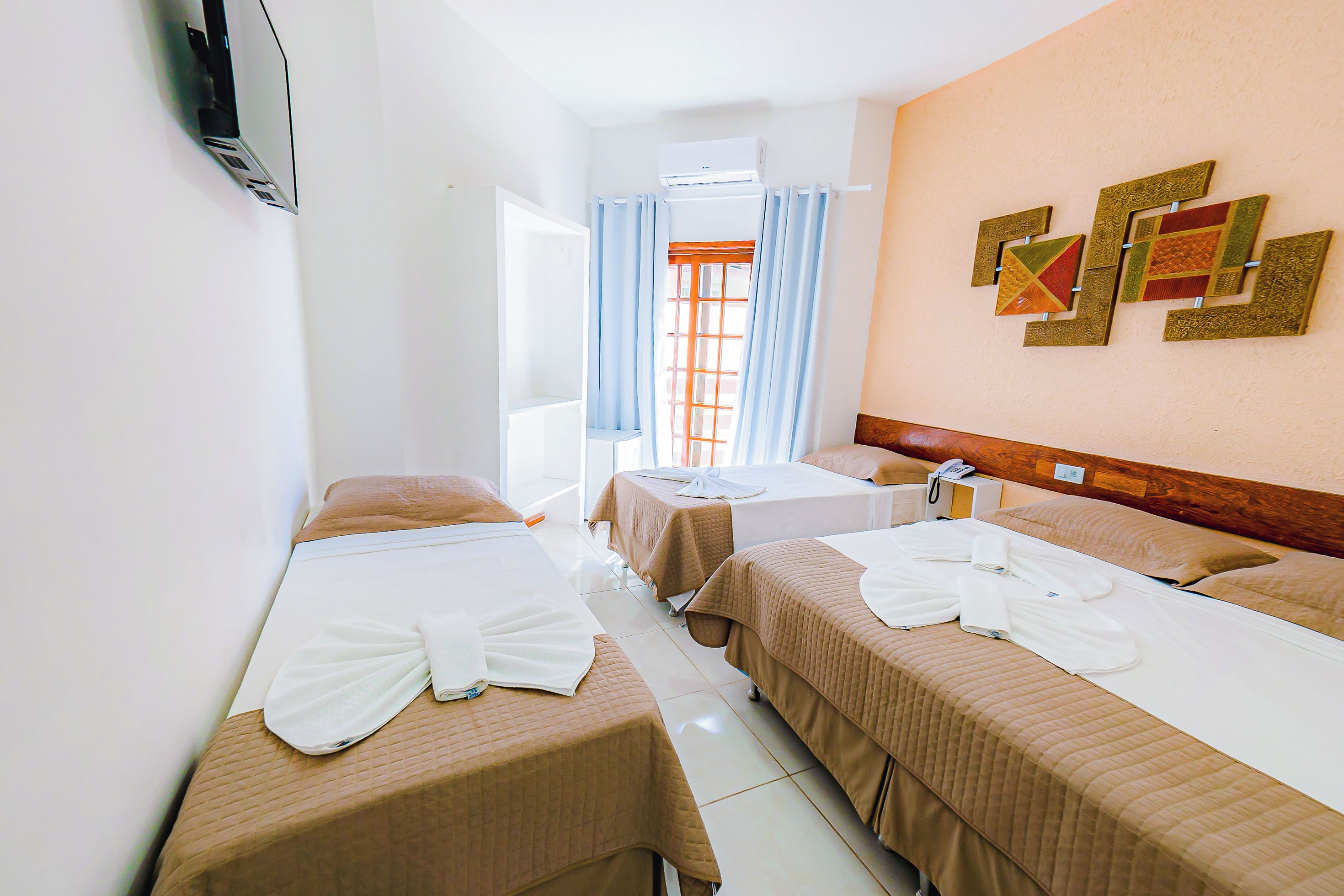 A hotel room with two beds, a wooden headboard, a wall-mounted air conditioner, and a window with curtains.