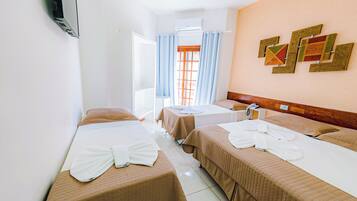 A hotel room with two beds, a wooden headboard, a wall-mounted air conditioner, and a window with curtains.