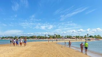 A beach with people walking and standing, palm trees, and a clear blue sky.
