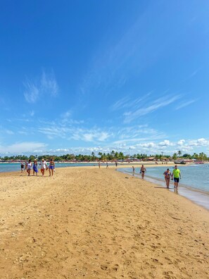 A beach with people walking and standing, palm trees, and a clear blue sky. - Bem Bahia Hotel (Santa Cruz Cabralia)