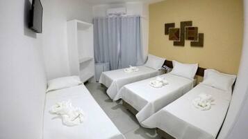 A hotel room with three single beds, a TV mounted on the wall, and a window with curtains.