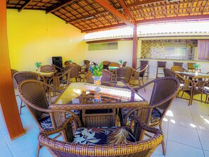 A covered outdoor dining area with wicker furniture and a glass table. - Bem Bahia Hotel (Santa Cruz Cabralia)