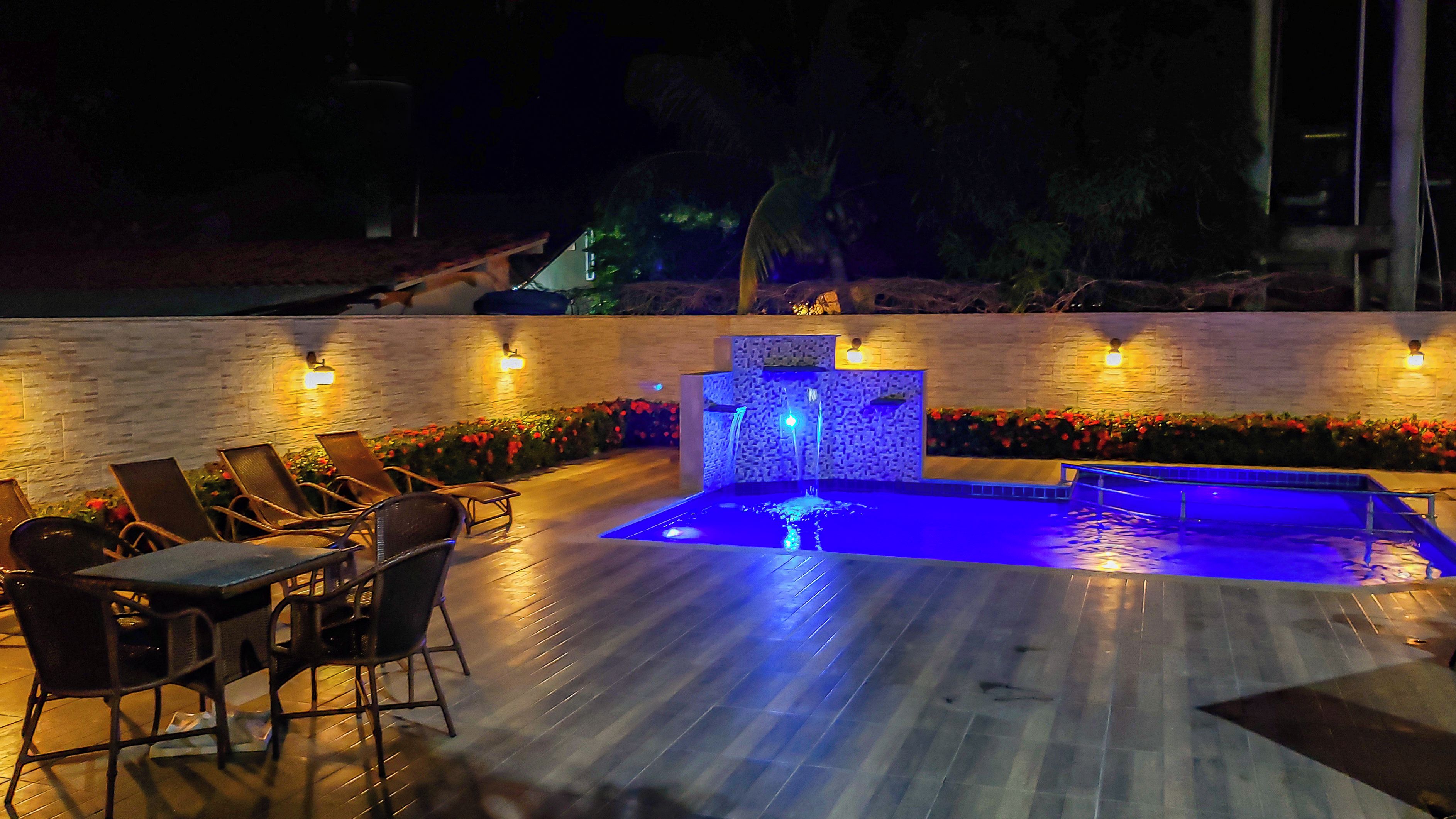 Zona de piscina con fuente, sillas de descanso y pared de piedra con iluminación.
