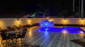 A pool area with a water feature, lounge chairs, and a stone wall with lights. - Bem Bahia Hotel (Santa Cruz Cabralia)