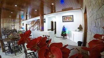 A spacious dining area with a high ceiling and wooden beams, a staircase leading to an upper level, and a Christmas tree with lights.