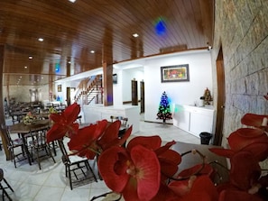 A spacious dining area with a high ceiling and wooden beams, a staircase leading to an upper level, and a Christmas tree with lights. - Bem Bahia Hotel (Santa Cruz Cabralia)