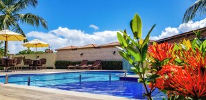 A swimming pool with lounge chairs and umbrellas, surrounded by palm trees and a clear sky. - Bem Bahia Hotel (Santa Cruz Cabralia)