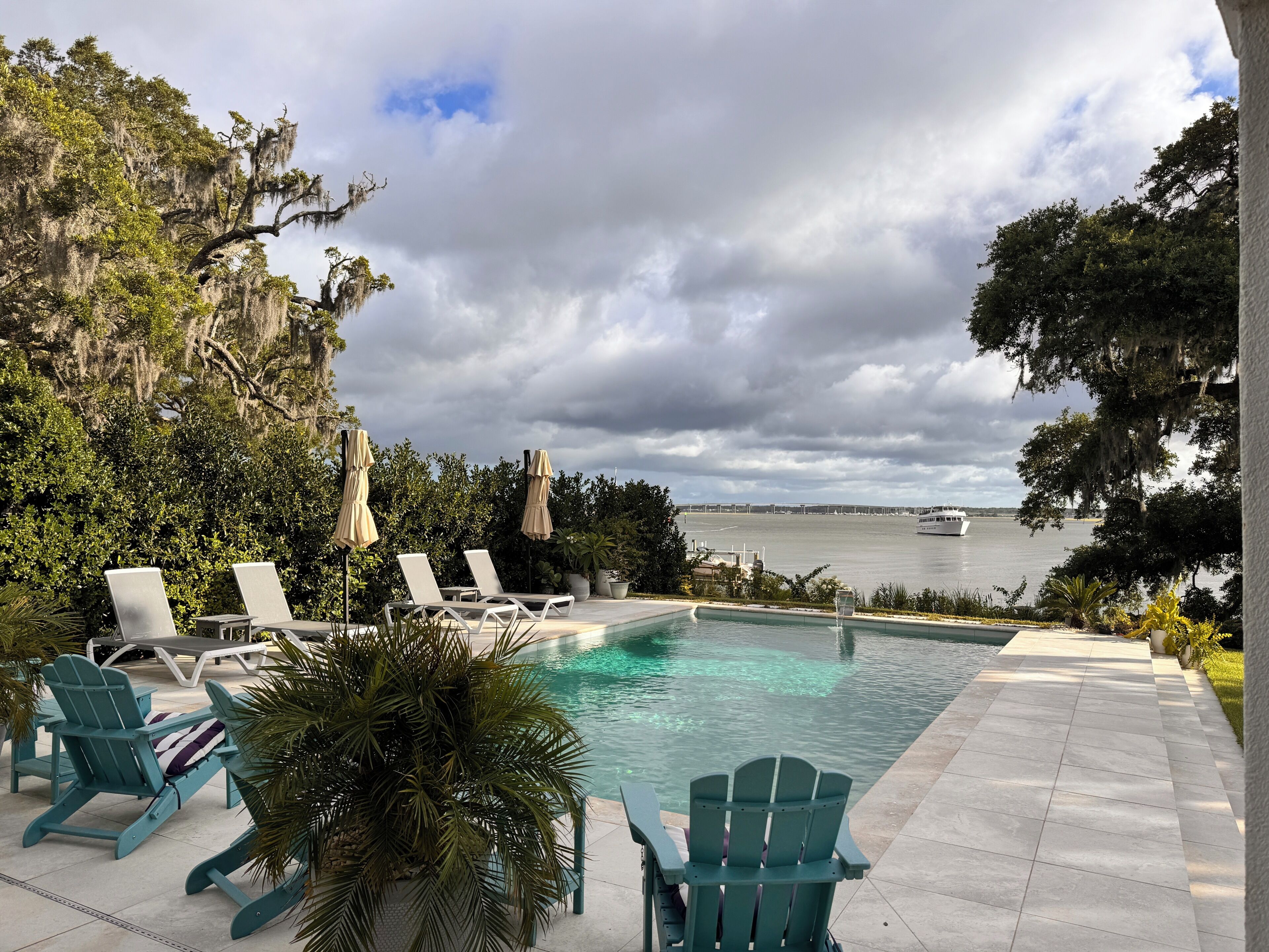 A pool area with lounge chairs and a view of the water.