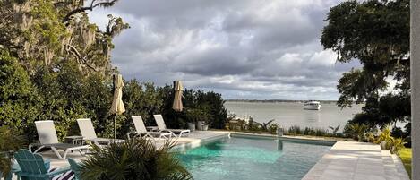 A pool area with lounge chairs and a view of the water.