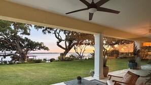 A covered patio with outdoor furniture, a view of the water, and a large tree.