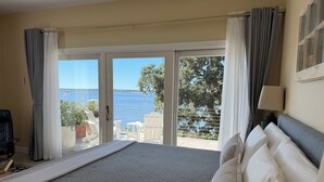 A hotel room with a bed, a desk, a chair, and a view of the sea.