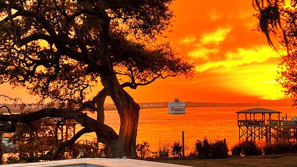 A pool area with a sunset view, a dock, and a boat in the distance.