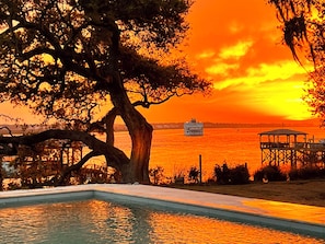 Une piscine avec vue sur le coucher de soleil, un quai et un bateau visible au loin.