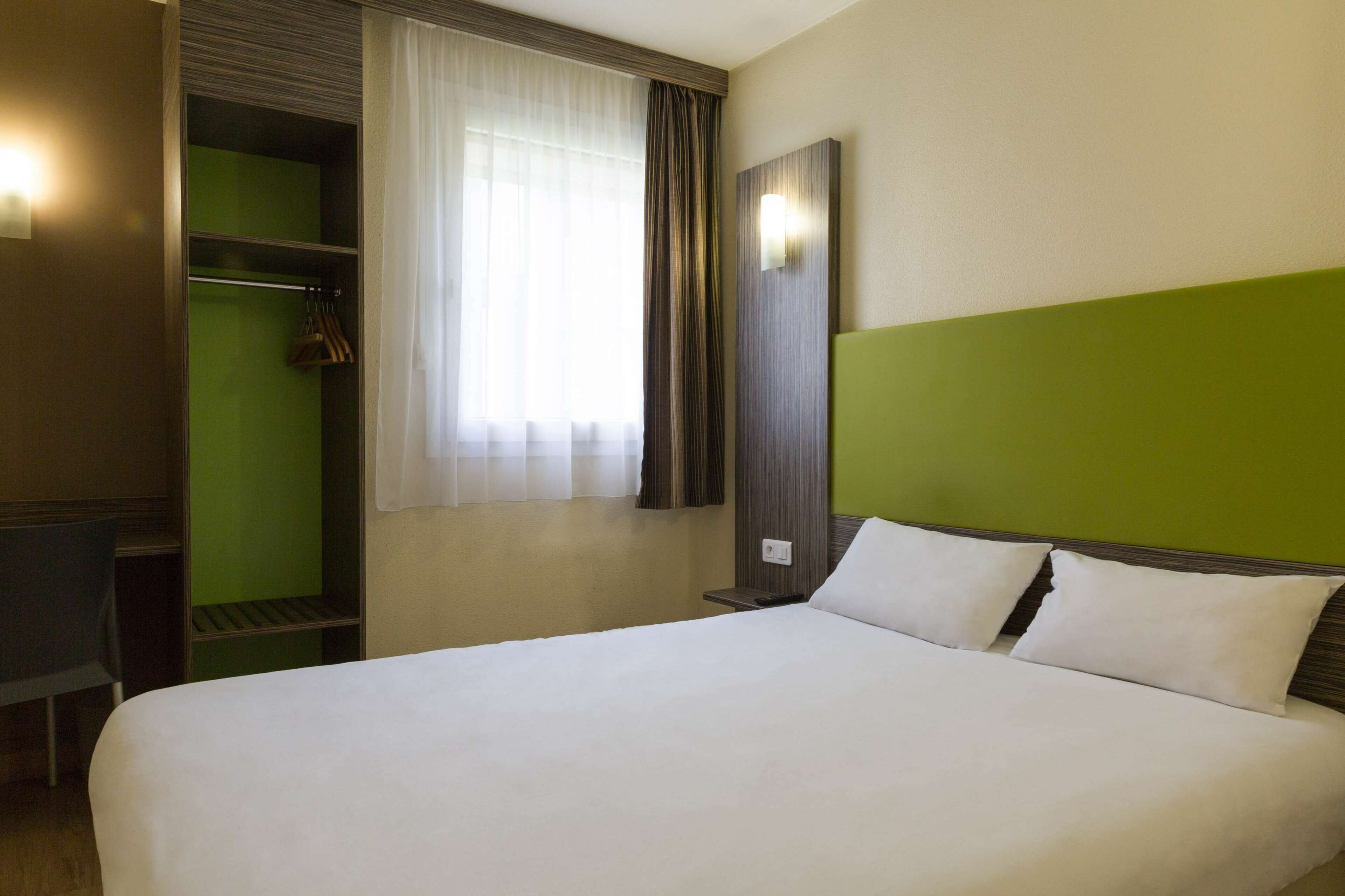 Hotellihuone, jossa on sänky, vihreä tehosteseinä, vaatekaappi ja ikkuna, jossa on verhot.