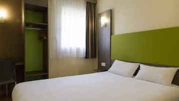 Hotellihuone, jossa on sänky, vihreä tehosteseinä, vaatekaappi ja ikkuna, jossa on verhot.
