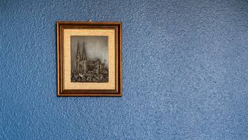 A bed with white bedding against a blue wall, a framed picture of a building above it.