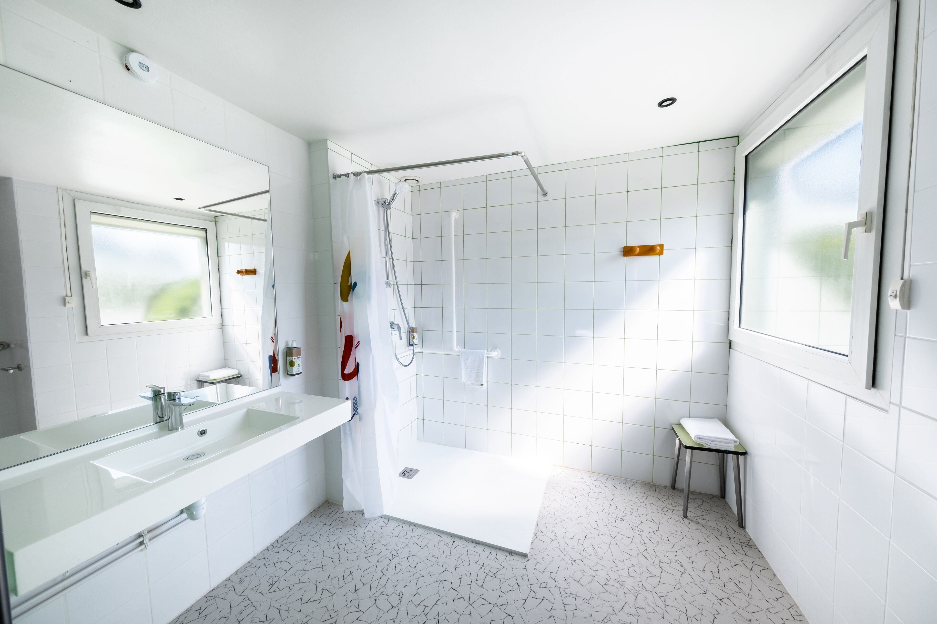 A modern bathroom with a glass-enclosed shower, a large mirror, and a white tiled floor.