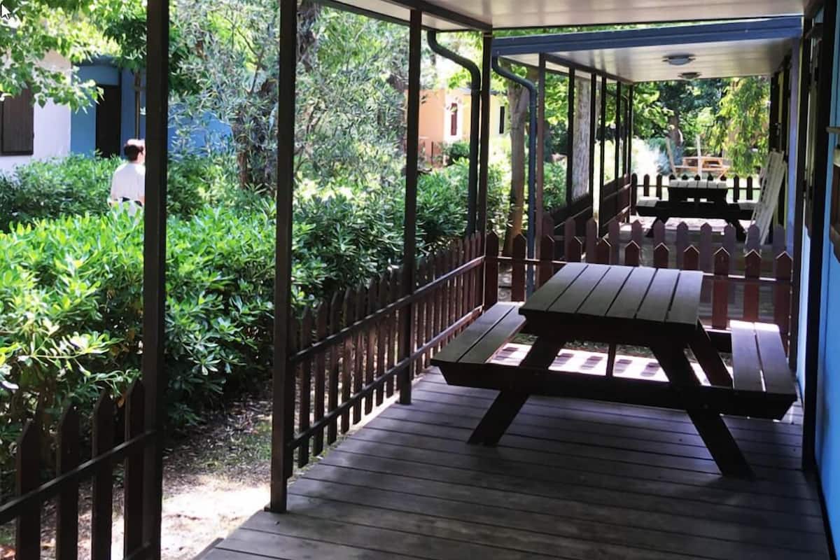 Un espace extérieur abrité, doté d’une terrasse en bois, de tables de pique-nique et d’une clôture en métal.