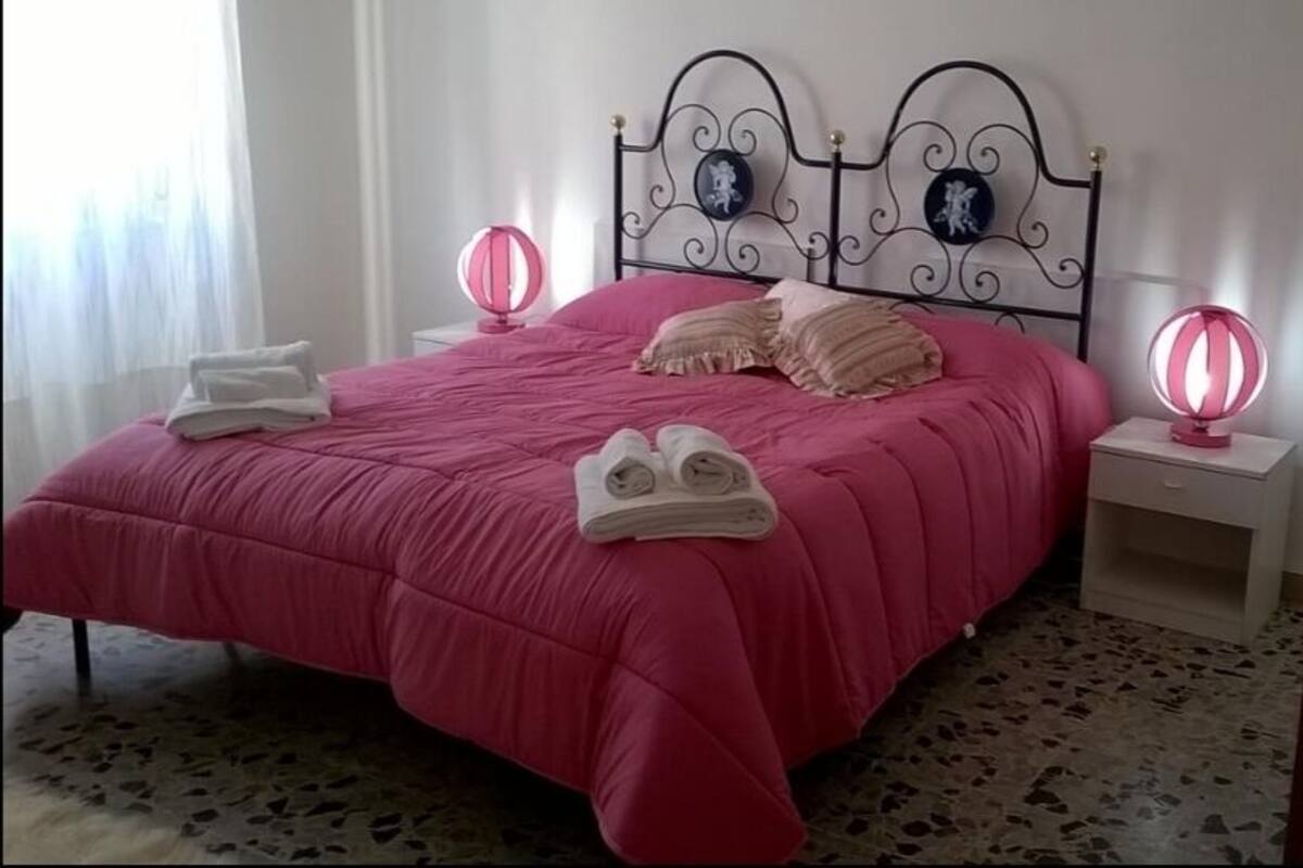 A neatly made bed with pink bedding and two decorative wall sconces.