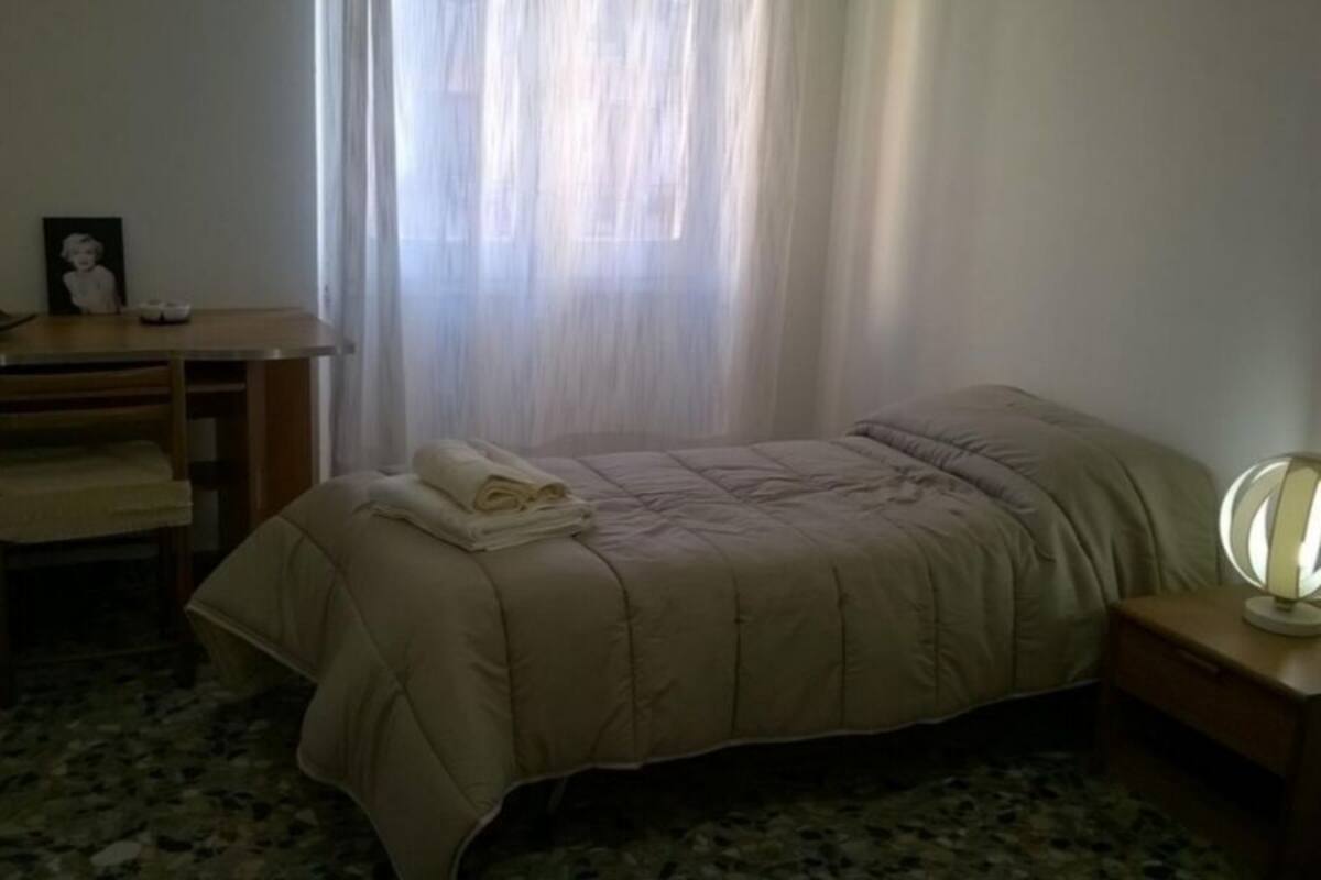 A bedroom with a bed, a desk, and a nightstand.
