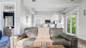 A living room with a leather sofa, a wooden coffee table, and a view of the kitchen and outside.