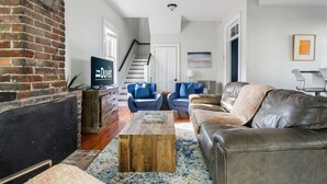 A living room with a brick wall, a wooden coffee table, a leather sofa, and blue armchairs.