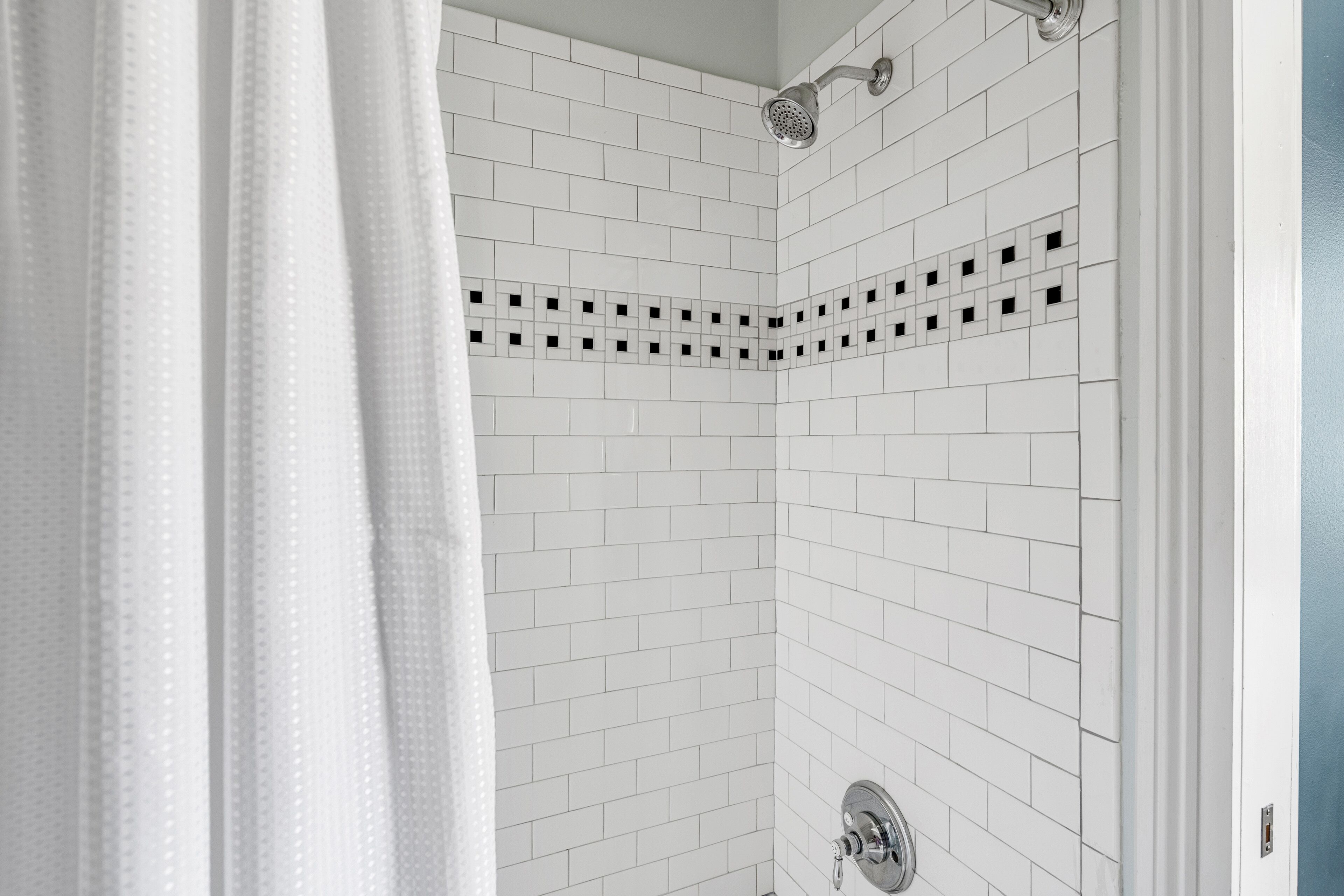 Ducha con azulejos blancos y cabezal.