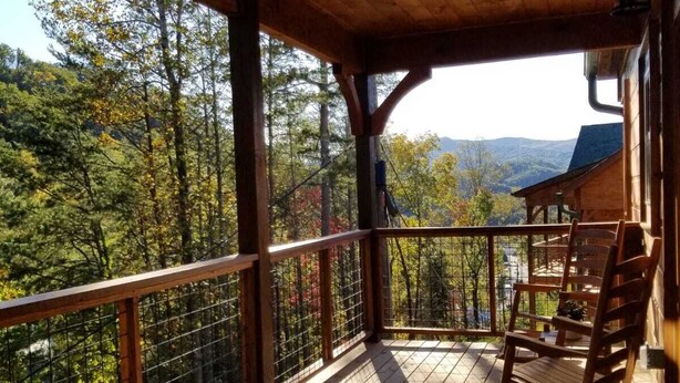 A wooden deck with a railing, a rocking chair, and a view of a forest and mountains.