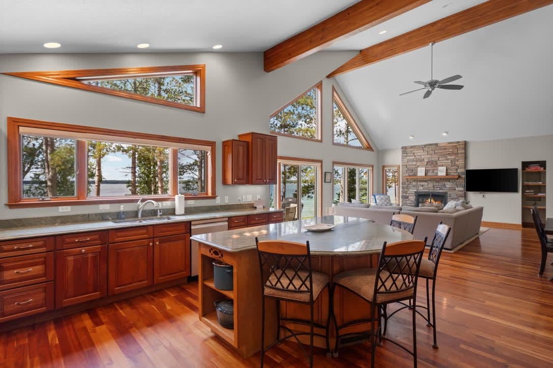 A spacious kitchen with large windows, wooden cabinets, and a central island with chairs.
