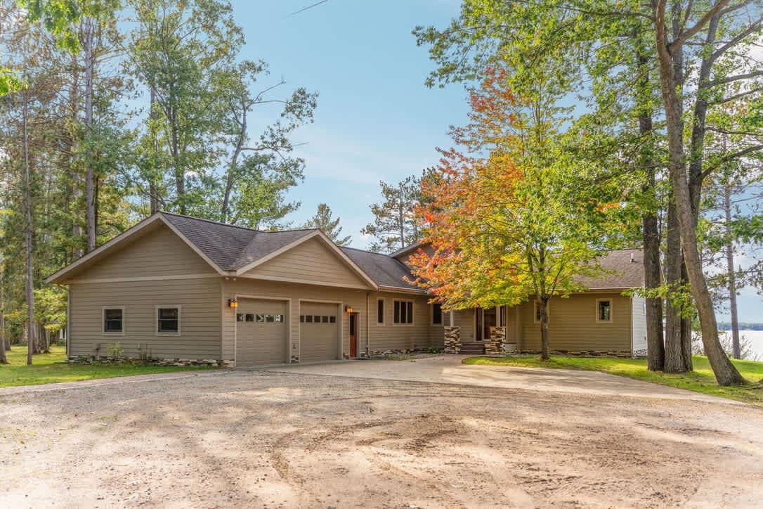 A two-story house with a garage, a covered porch, and a driveway leading to a gravel area.