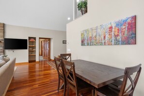 A dining area with a wooden table and chairs, a flat-screen TV, and a colorful painting on the wall. - Sunset View | Superior West Twin Lake Home (Lewiston)