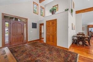 A spacious interior with a large wooden door, a dining area with a table and chairs, and a patterned rug on the floor. - Sunset View | Superior West Twin Lake Home (Lewiston)