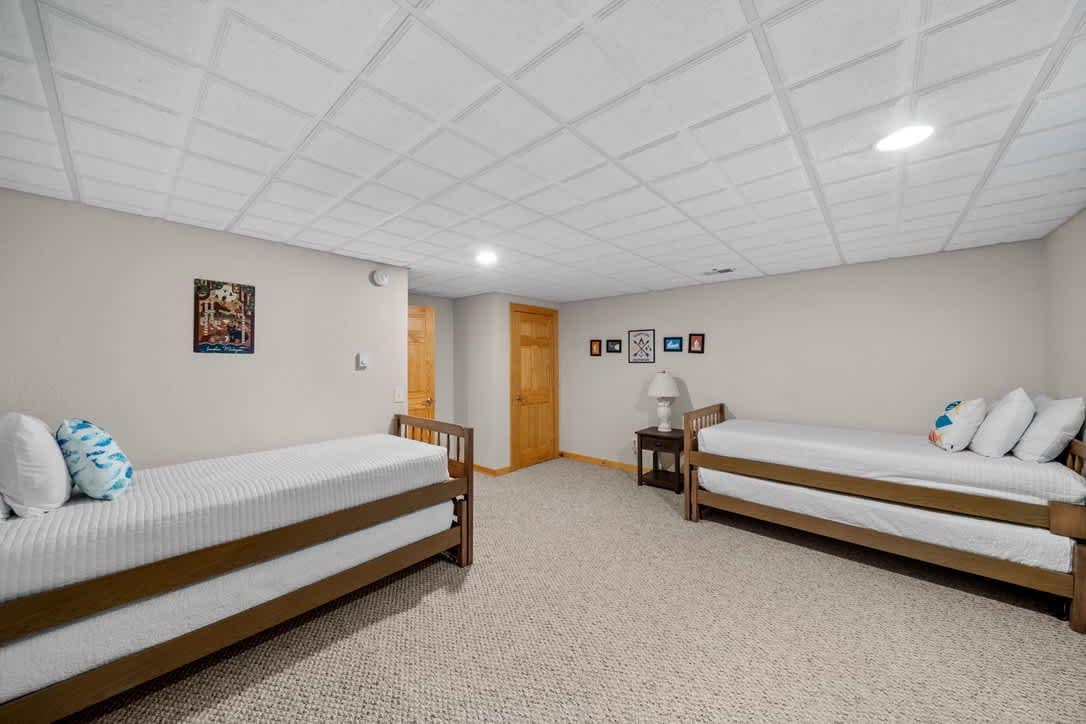 A room with two single beds, a small table, and a door leading to another room.