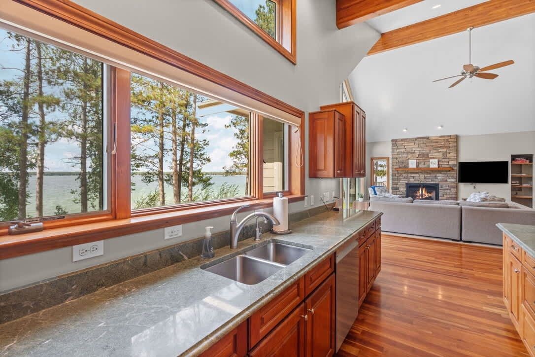 A modern kitchen with a large window overlooking a lake, wooden cabinets, and a built-in fireplace.