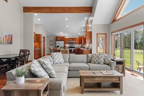A modern living room with a sectional sofa, a coffee table, and a dining area with wooden chairs.