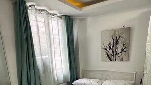 A bedroom with a bed, curtains, a nightstand, and a wall art piece. - Cozy Familia Apartment Studio Type (Cagayan de Oro City)