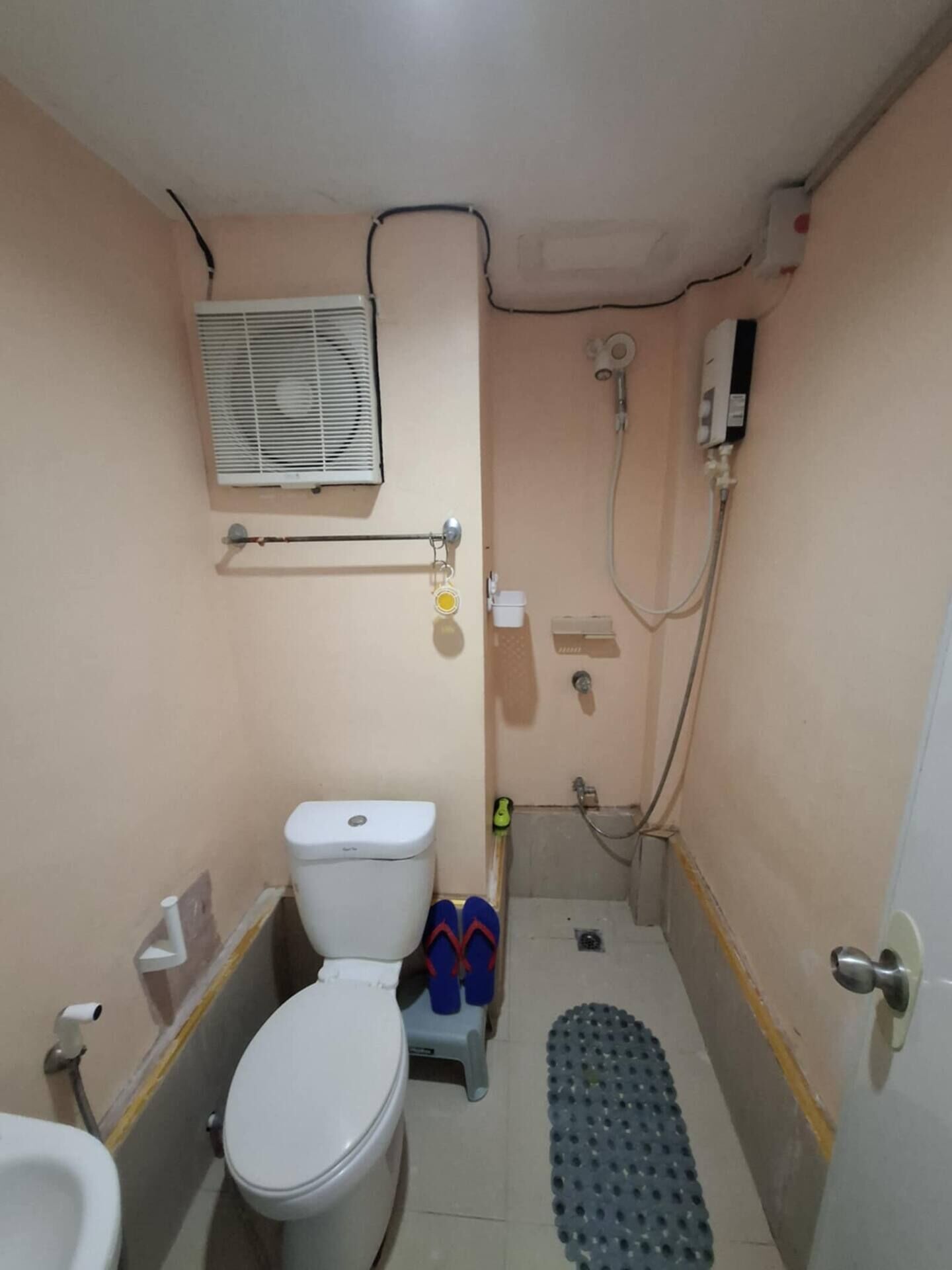 A small bathroom with a toilet, a shower, and an air conditioning unit mounted on the wall.