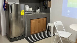 A compact kitchen with a refrigerator, wooden cabinets, a sink, and a small dining area with a chair. - Cozy Familia Apartment Studio Type (Cagayan de Oro City)