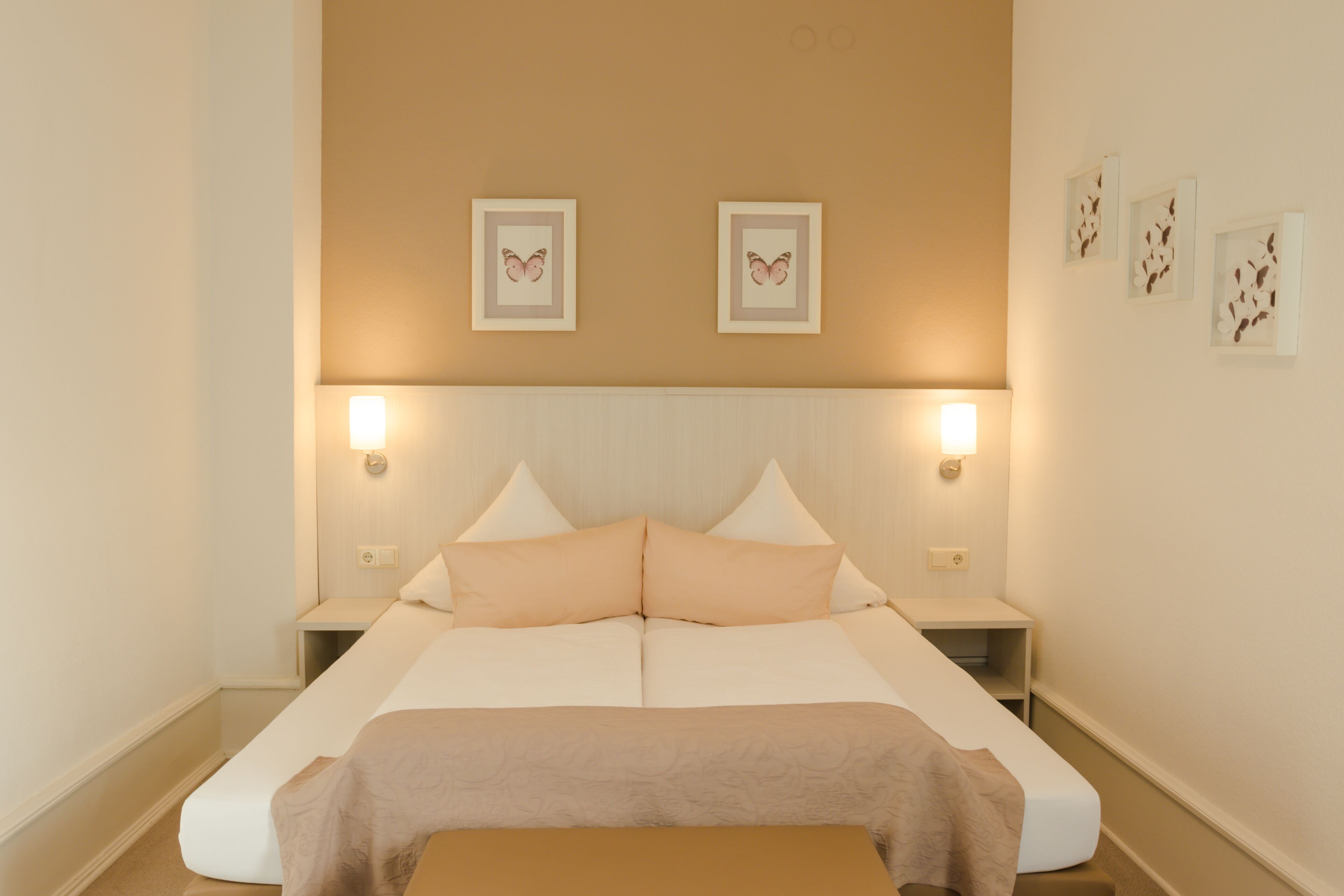 A bedroom with a large bed, two bedside tables, and wall-mounted lights.