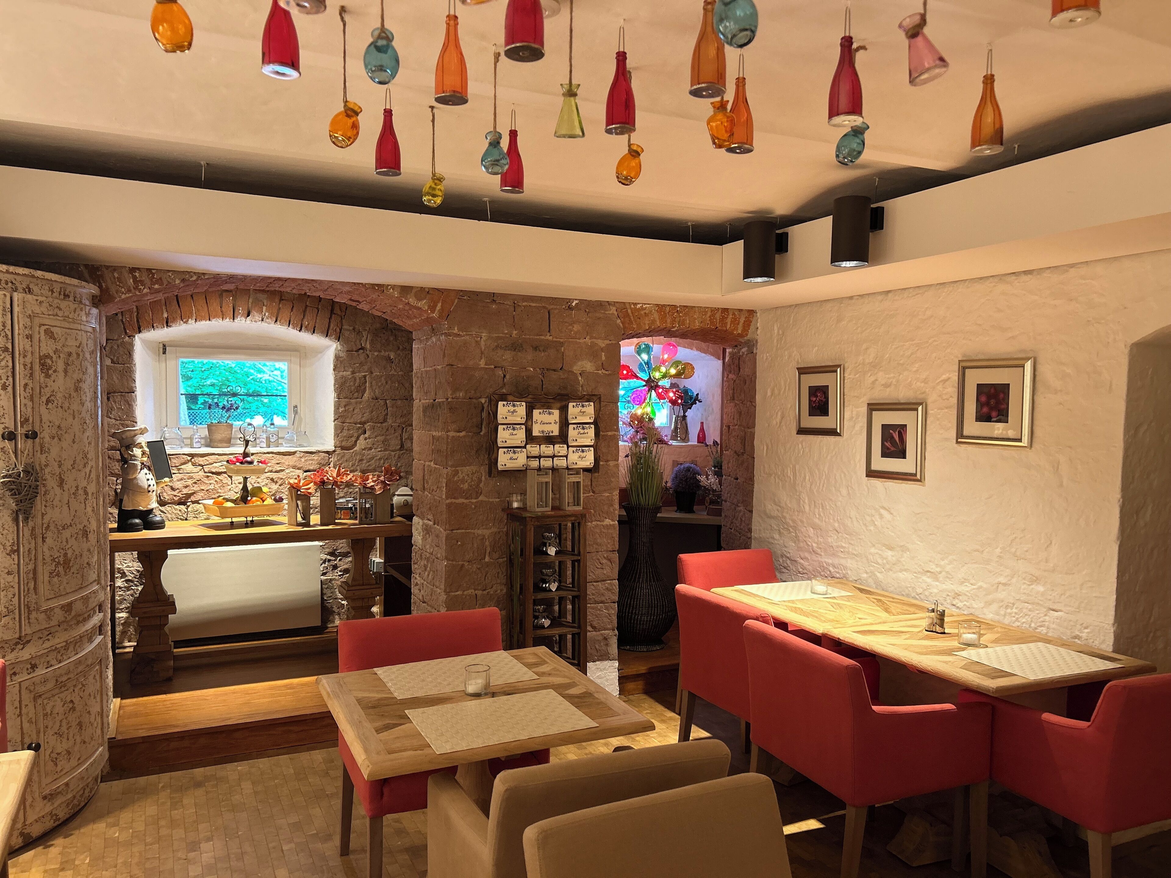 A cozy dining area with a wooden table and red chairs, a stone wall, and a window with a view.