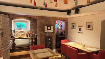 A cozy dining area with a wooden table and red chairs, a stone wall, and a window with a view.